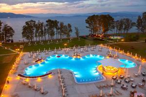 Ein abendlicher Blick auf den Außenbereich des Louis Kerkyra Blue Hotels mit Swimmingpool, Sonnenliegen und Bäumen.