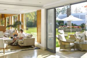 Zwei Personen sitzen in der Lounge des Louis Kerkyra Blue Hotels mit Blick auf eine Gartenterrasse.