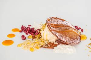 Dessert von DeLight Boutique Hotel mit Eis, karamellisierten Blättern und Früchten auf weißem Teller