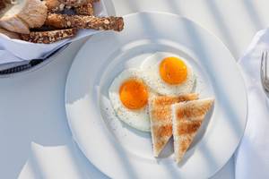 Frühstück mit zwei Spiegeleiern, Toast und Brot auf einem weißen Teller.
