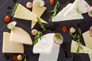 Verschiedene Käsesorten auf einem schwarzen Teller serviert, mit Radieschen, Rucola und Haselnüssen garniert, DeLight Boutique Hotel