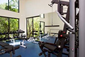 Fitnessraum im Occidental Tamarindo Hotel mit großen Fenstern und Blick auf Bäume.