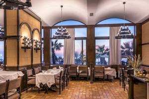 Innenansicht des Restaurants im Mitsis La Vita Beach Hotel mit runden Fenstern und Tischdekoration.