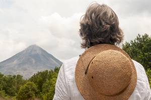 Person in Hut blickt auf Vulkan und Himmel im Hintergrund