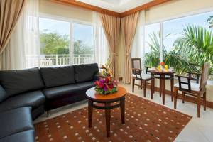 Wohnzimmer im Occidental Tamarindo Hotel mit schwarzem Sofa, Tisch und großem Fenster mit Blick auf Palmen