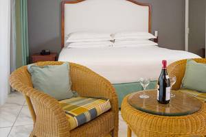 Ein elegantes Zimmer im Occidental Tamarindo Hotel mit zwei Rattanstühlen, einem Tisch, einer Weinflasche und zwei Weingläsern neben einem großen Bett.