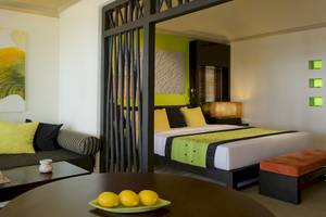 Innenansicht eines Zimmers im Dhawa Ihuru Hotel mit Bett, Couch, Tisch und Gemälden an der Wand.