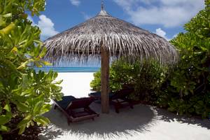 Zwei Sonnenliegen unter einem Strohhut auf dem weißen Sandstrand von Coco Palm Dhuni Kolhu.