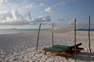 Strand des Coco Palm Dhuni Kolhu Hotels mit Sonnenliegen unter einem Segel