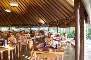 Innenansicht des Coco Palm Dhuni Kolhu Restaurants mit runden Tischen, Stühlen und blauen Gläsern.