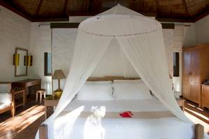 Ein Bett im Coco Palm Dhuni Kolhu Hotel mit einem weißen Baldachin und einem roten Spielzeug auf dem Bett.