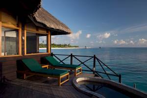 Terrasse des Coco Palm Dhuni Kolhu Hotels mit zwei Liegen und Ausblick auf das Meer.