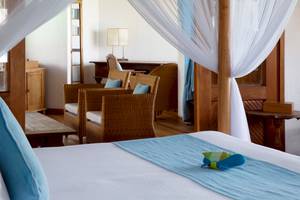 Schlafzimmer im Coco Palm Dhuni Kolhu Hotel mit vier Posterbett, zwei Stühlen, Schreibtisch und Lampe