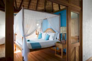 Schlafzimmer im Coco Palm Dhuni Kolhu Hotel mit Himmelbett, blauen Wänden und Holzboden