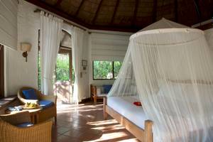 Ein Schlafzimmer im Coco Palm Dhuni Kolhu Hotel mit einem Bett unter einem Moskitonetz und zwei Stühlen.