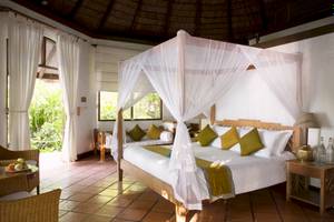 Coco Palm Dhuni Kolhu Hotel Schlafzimmer mit zwei Himmelbetten, Vorhängen, Kissen, Tisch und Lampen.