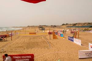 Ein Volleyballspielfeld am Strand mit Werbetafeln und einer Person, die darauf zugeht.