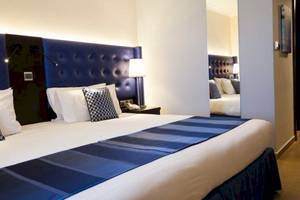 Ein geräumiges Hotelzimmer mit blauen Kopfteilen und weißen Kissen, AX The Victoria Hotel.
