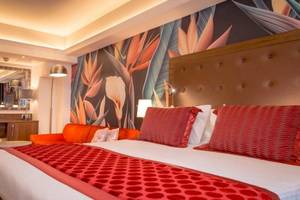 Schlafzimmer im AX The Victoria Hotel mit tropischen Wandmalereien, einem großen Bett, zwei roten Stühlen und einem Couchtisch.