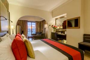 Zimmer im AX The Victoria Hotel mit Bett, Kissen, Schreibtisch, Sessel, Lampe und Balkon