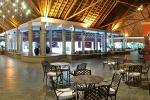Hotellobby des Catalonia Playa Maroma mit Tischen, Stühlen und einer Bar.