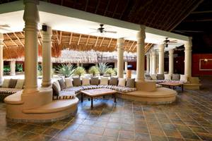 Innenbereich des Hotels Catalonia Playa Maroma mit Sitzbereichen, Tischen und Deckenventilatoren.