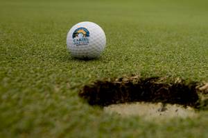 Ein Golfball mit dem Logo Caribe Golf Club liegt auf einem Golfplatz neben einem Loch.