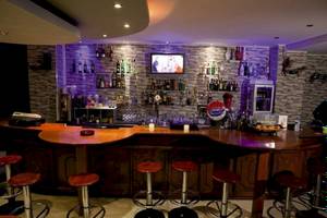 Innenansicht der Bar im Sunny Days Hotel mit einer Theke, roten Stühlen, vielen Flaschen und einem Fernseher