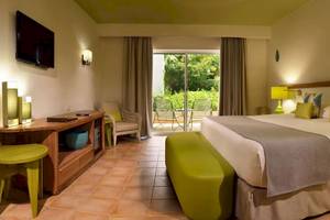 Hotelzimmer im Catalonia Playa Maroma mit Doppelbett, grünen Stühlen und Tisch, Fernseher und Balkonzugang.
