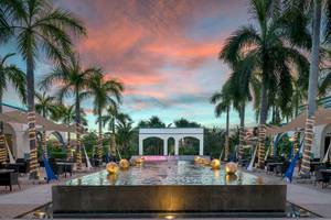Gartenbereich des Ocean Maya Royale Hotels bei Sonnenuntergang mit Brunnen und Palmen