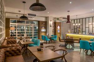 Innenbereich des Ocean Maya Royale Hotels mit modernen Möbeln, blauen Stühlen, Holztischen und einer Bar.