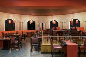 Innenbereich des Ocean Maya Royale Hotels mit Restaurantbereich, roten Tischen und Stühlen sowie orangefarbenen Lampen.
