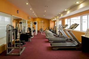 Fitnesscenter im Ocean Maya Royale Hotel mit roten Teppichboden, Fitnessgeräten und Fenstern.