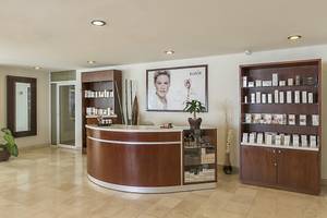 Empfangsbereich des Ocean Maya Royale Hotels mit Empfangstresen, BaBOR-Produkten und einer Frau auf Plakat.