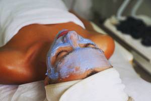 Frau mit blauer Gesichtsmaske liegt auf einem Behandlungstisch