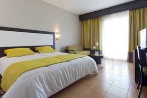 Hotelzimmer im El Mouradi Club Kantaoui mit Bett, gelben Kissen und grünen Vorhängen.