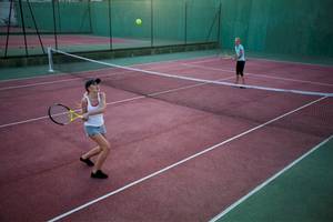Zwei Frauen spielen Tennis auf einem roten Tennisplatz mit einer Netz und einem Tennisball in der Luft.