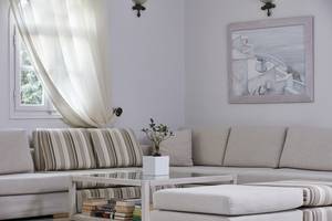 Wohnzimmer mit grauem Sofa, Couchtisch mit Büchern und einer Pflanze, neben einem Fenster mit Vorhang.