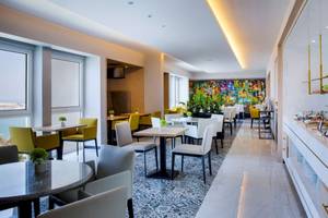 Innenansicht des Restaurants im Radisson Blu Hotel & Resort, Abu Dhabi mit Tischen, Stühlen und einer bunten Wandgestaltung.