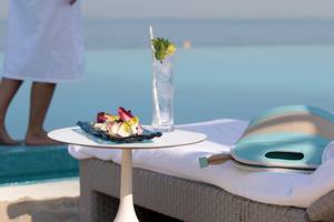 Person am Strand neben einem Tisch mit einem Getränk und einem Tablett mit Essen, Blick auf das Meer, Burj Al Arab Jumeirah