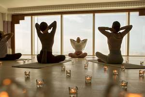 Yoga-Stunde im Burj Al Arab Jumeirah Hotel mit mehreren Frauen, die vor großen Fenstern praktizieren.