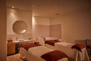 Ein Spa-Behandlungsraum mit zwei Massagetischen, einer Badewanne und einem Spiegel.