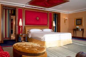 Schlafzimmer im Burj Al Arab Jumeirah Hotel mit rotem Wanddesign, goldenem Bett und zwei Nachttischen.