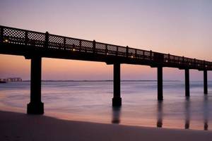Jumeirah Al Qasr Pier bei Sonnenuntergang mit beleuchteten Säulen und blauem Wasser.