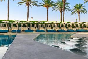 Der Poolbereich des W Ibiza mit Loungesesseln, Sonnenschirmen und Palmen im Hintergrund.