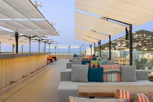 Terrasse des W Ibiza Hotels mit Sofas, Kissen und Sonnenschirmen mit Blick auf das Meer und die Stadt