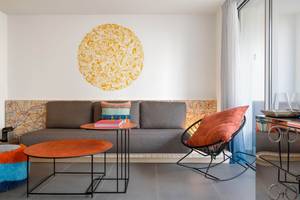 Innenansicht des Wohnzimmers im W Ibiza Hotel mit grauem Sofa, orangefarbenem Stuhl und runden Tischen.