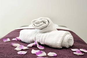 Zwei weiße Handtücher sind auf einem violetten Handtuch auf einem Bett gefaltet, mit rosa Blumenblättern verstreut.