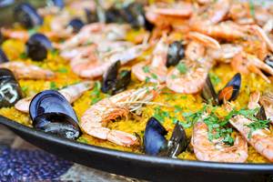 Eine große Platte Paella mit Garnelen und Muscheln, serviert auf einem runden Tisch.