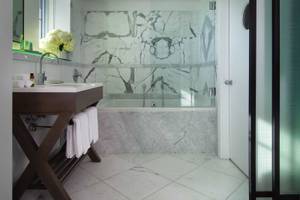 Badezimmer im Victor South Beach Hotel mit Marmorwänden, Badewanne und modernem Waschtisch.